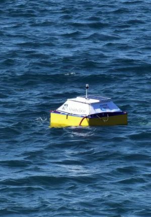 A small yellow and white autonomous survey vessel with a solar panel alone on choppy dark blue water.