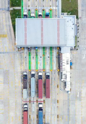 Overhead aerial view of a logistics terminal with color-coded inspection lanes, gantry scanners, and rows of container trucks parked on marked concrete.